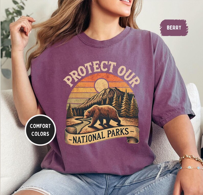 May include: A purple t-shirt with a vintage-style graphic of a bear in a forest with the text "Protect Our National Parks".