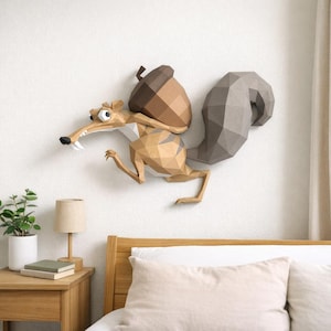 Pode incluir: Uma escultura de parede em papel low-poly de um esquilo com uma grande bolota castanha. O esquilo apresenta facetas geométricas em tons de bege e castanho claro, um olho branco proeminente e uma grande cauda cinzenta texturizada na parede.