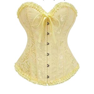 Puede incluir: Un corsé amarillo pálido con escote corazón y un delicado estampado floral. El corsé presenta una fila de cierres de gancho y ojo en la parte delantera y un lazo decorativo. Los bordes superior e inferior están adornados con volantes.