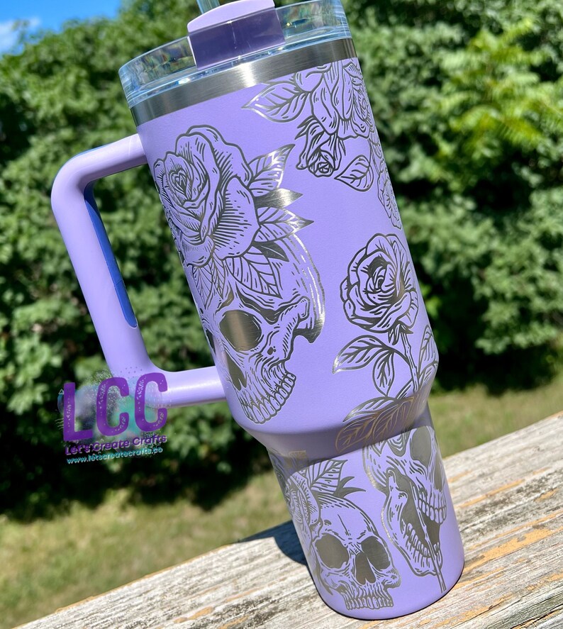 May include: A purple stainless steel tumbler with a black and silver skull and rose design. The tumbler has a handle and a lid. The text "Let's Create Crafts" and "www.letscreatecrafts.co" is on the handle.