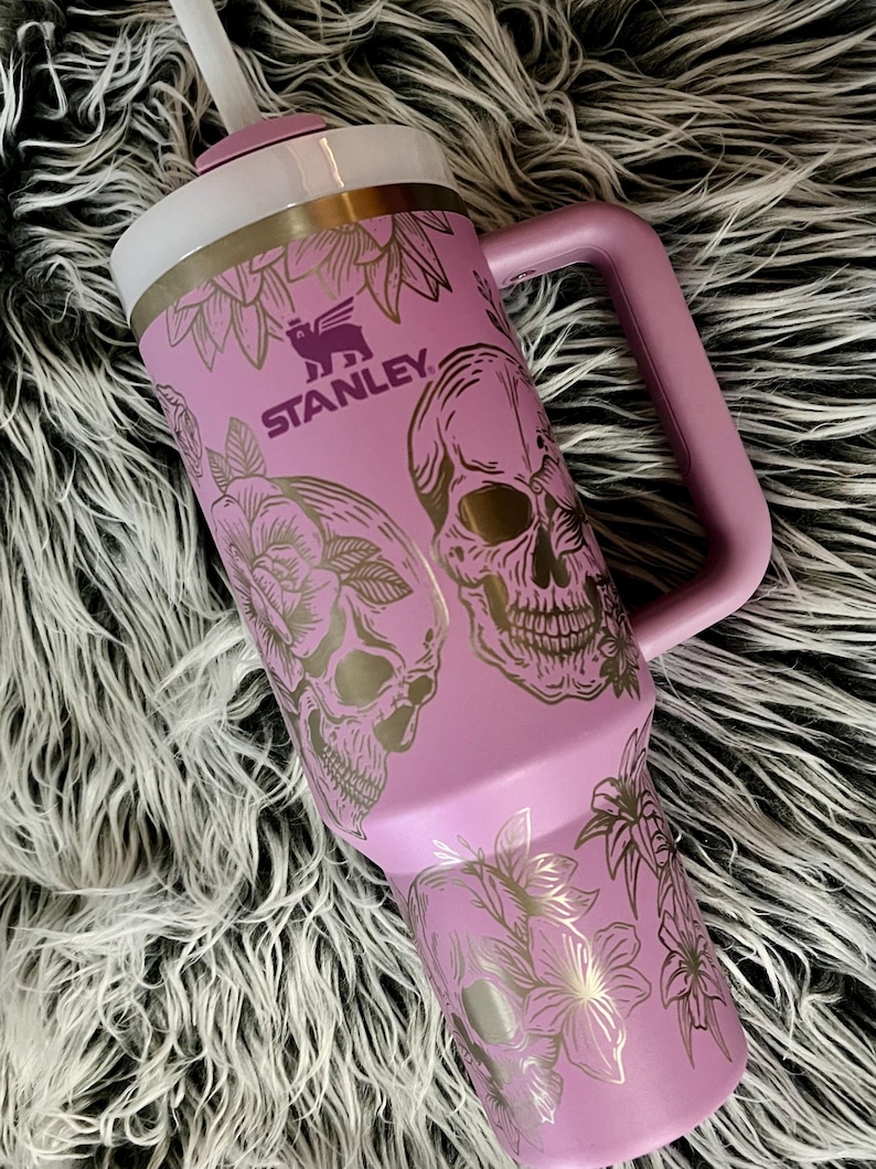 May include: A purple stainless steel travel mug with a handle. The mug has a floral and skull design with the word "STANLEY" printed on the side.