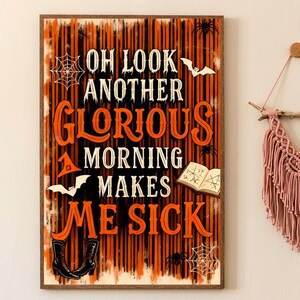 May include: A framed Halloween-themed sign with the text "OH LOOK ANOTHER GLORIOUS MORNING MAKES ME SICK" in orange and white. The background is orange and black vertical stripes. Decorative elements include bats, spiders, and a book.