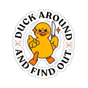 Può includere: Un'anatra gialla di cartone animato che tiene un coltello con il testo "Duck Around And Find Out" in un cerchio attorno ad essa.