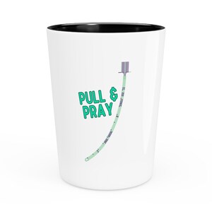 May include: White ceramic mug with a black rim. The mug has a green medical IV tube with a purple connector and the text "PULL & PRAY" in green.