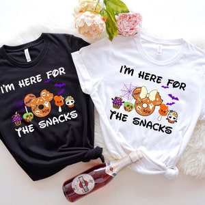 May include: Two black and white t-shirts with a Halloween theme. The shirts feature a Mickey Mouse and Minnie Mouse head with a donut and the text "I'm here for the snacks".