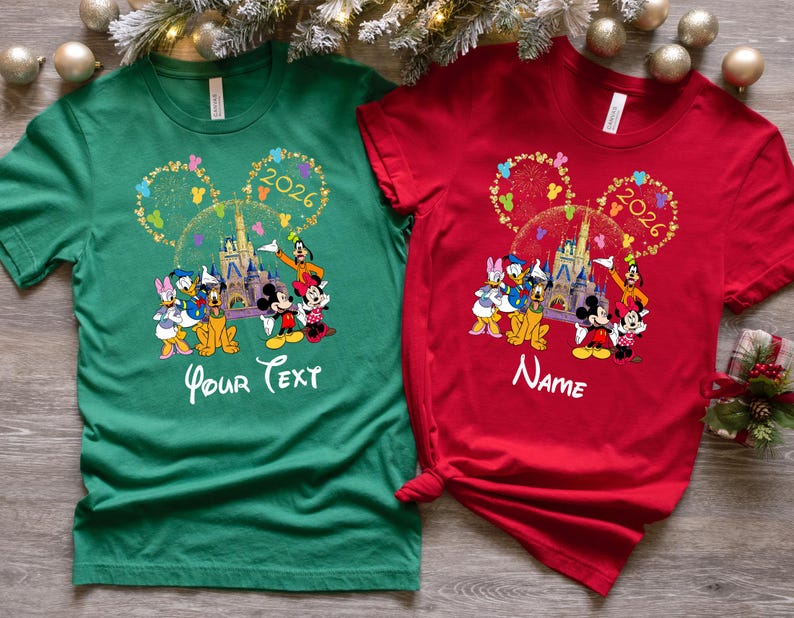 Puede incluir: Dos camisetas, una verde y otra roja, con un dise&ntilde;o de Disney. El dise&ntilde;o incluye orejas de Mickey Mouse, un castillo y varios personajes. La camiseta verde tiene "Your Text", la camiseta roja tiene "Name", y el a&ntilde;o 2026.