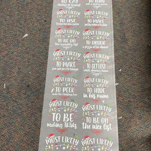 May include: A set of 10 gray Christmas-themed gift tags with white text and colorful lights. The tags say "Most Likely To..." and include phrases like "Eat chocolate for breakfast", "Buy out a dairy farm", "Be on the naughty list", "Order a pizza at ten dinner", "Peek under the Christmas tree", "Hide in his room", "Be making TikToks", "Be on the nice list", "Drink all the vodka", "Have a Christmas party", "Drink Santa's beer", and "Eat Santa's cookies".