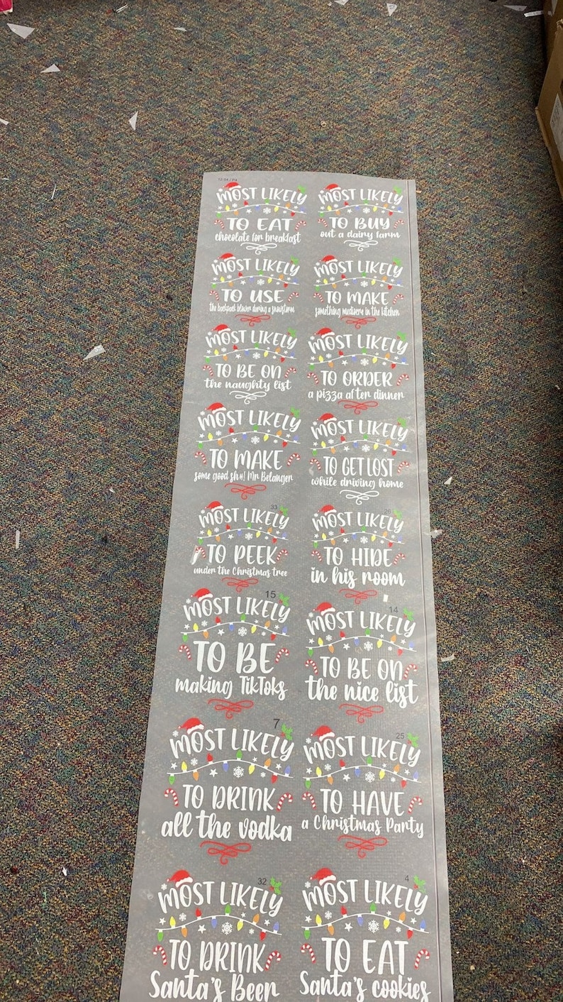 May include: A set of 10 gray Christmas-themed gift tags with white text and colorful lights. The tags say "Most Likely To..." and include phrases like "Eat chocolate for breakfast", "Buy out a dairy farm", "Be on the naughty list", "Order a pizza at ten dinner", "Peek under the Christmas tree", "Hide in his room", "Be making TikToks", "Be on the nice list", "Drink all the vodka", "Have a Christmas party", "Drink Santa's beer", and "Eat Santa's cookies".