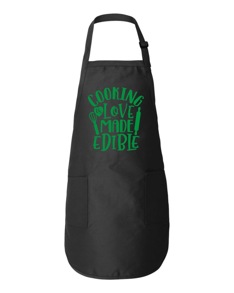 Peut inclure: Tablier noir avec un motif vert qui dit "Cooking Love Made Edible" avec un fouet et un rouleau &agrave; p&acirc;tisserie.