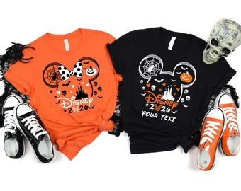 May include: An orange t-shirt and a black t-shirt, each featuring a graphic of a Mickey Mouse silhouette filled with a castle, pumpkins, bats, and skulls. The orange shirt has a polka dot bow, while the black shirt includes the text Disney 2026 YOUR TEXT.