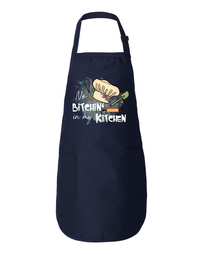 May include: A navy blue kitchen apron with a white pocket and a graphic that says "No Bitchin' in my Kitchen" with a chef's hat, rolling pin, spatula, and whisk.