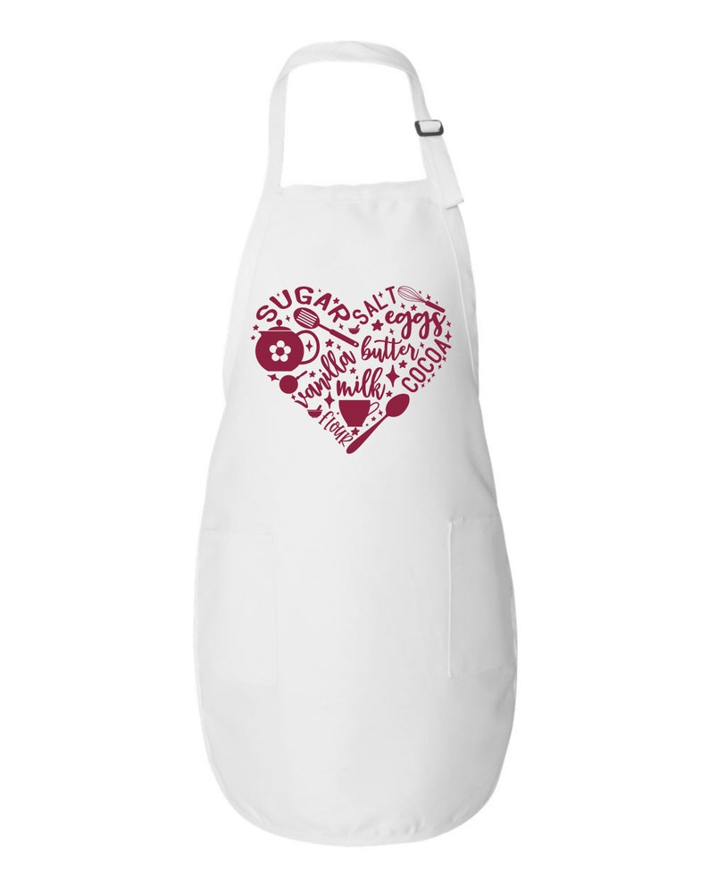 Peut inclure: Tablier blanc avec un motif de c&oelig;ur rouge comportant les mots "sucre, sel, &oelig;ufs, beurre, cacao, vanille, lait, farine" et des ic&ocirc;nes de p&acirc;tisserie.