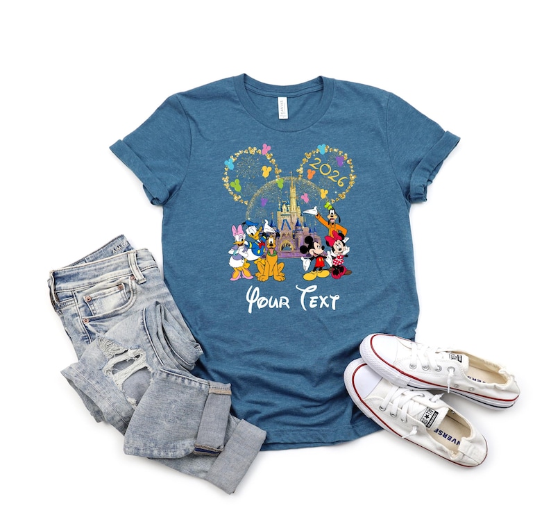 Puede incluir: Una camiseta azul con un dise&ntilde;o de Disney con Mickey Mouse, Minnie Mouse, Donald Duck y otros personajes. El dise&ntilde;o incluye el texto "2026" y "Your Text". La camiseta se combina con vaqueros azules y zapatillas blancas.