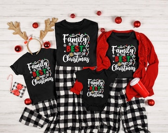 May include: A collection of black t-shirts and a baby bodysuit featuring the white, red, and green text "Family IS THE BEST PART OF Christmas" with string light graphics, paired with black and white plaid pyjama trousers and a red cardigan.