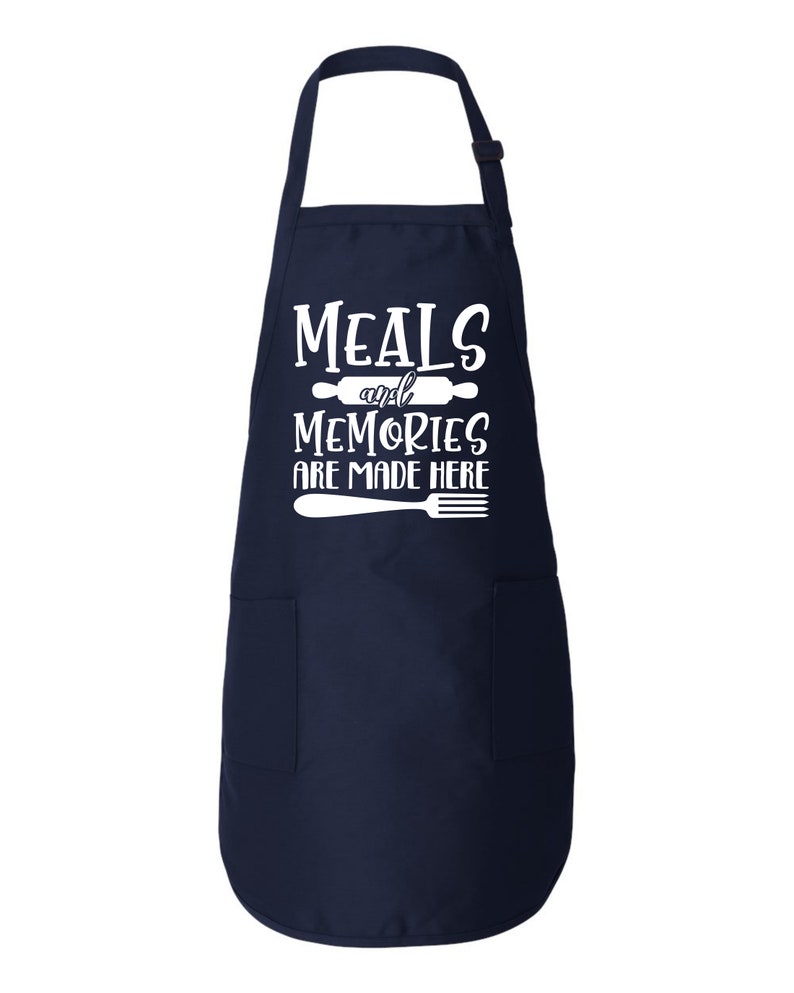 Peut inclure: Un tablier bleu marine avec un motif blanc qui dit "Meals and Memories are Made Here" avec un rouleau &agrave; p&acirc;tisserie et une fourchette.