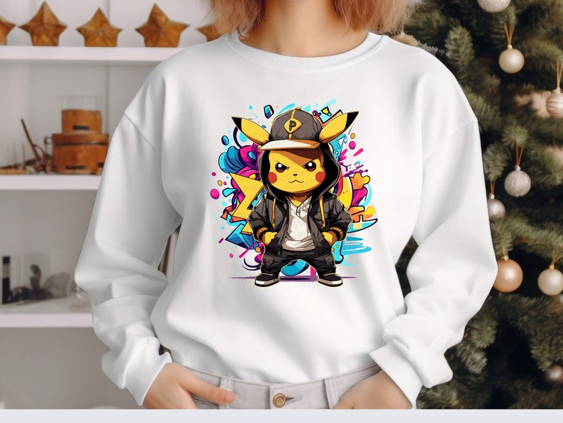 May include: White sweatshirt with a graphic print of a yellow Pikachu wearing a black and white hoodie, a black baseball cap with a white letter P, and black pants. The Pikachu is standing on a colorful background with abstract shapes.