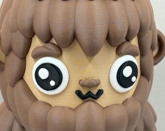 May include: A 3D-printed figurine of a cartoon Bigfoot, featuring a light brown face, dark brown fur, and large black and white eyes. The figurine has a friendly expression and a detailed, textured design.