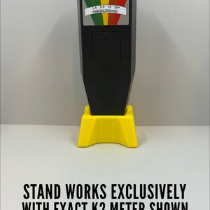 May include: A black K2 meter with a yellow stand. The meter has a color-coded display with readings from 1.5 to 20+ milliGAUSS. The text on the image reads: "STAND WORKS EXCLUSIVELY WITH EXACT K2 METER SHOWN *** K2 METER NOT INCLUDED ***".
