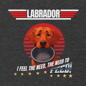 Puede incluir: Camiseta gris oscuro con un perro Labrador sosteniendo un cuenco. El diseño incluye la palabra "LABRADOR" encima del perro y la frase "I FEEL THE NEED, THE NEED TO FEED!" debajo, con estrellas.