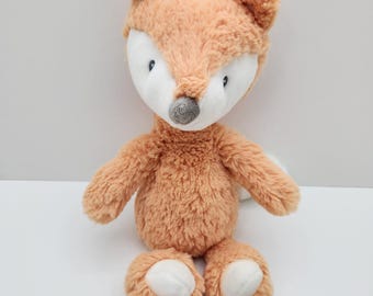 May include: A plush fox toy with soft, orange fur, white accents on the face and paws, and a gray nose. The stuffed animal has a friendly expression and is designed for children.