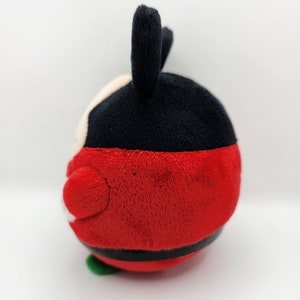 May include: Red and black plush toy with a round body and two black ears. The toy has a white face with black eyes and a black mouth.