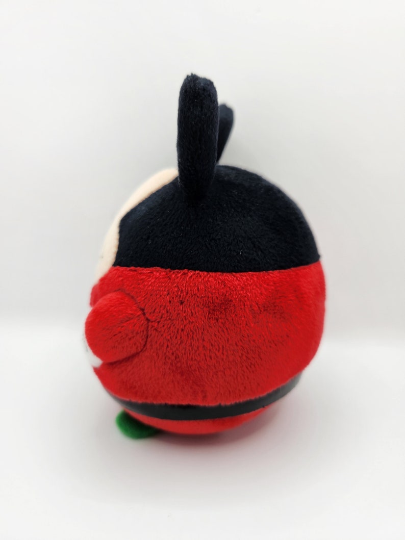May include: Red and black plush toy with a round body and two black ears. The toy has a white face with black eyes and a black mouth.