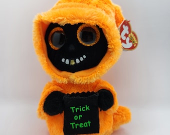 May include: Orange and black plush ghost holding a black bag with the text "Trick or Treat" in green. The ghost has large, glittery eyes and a toothy grin.