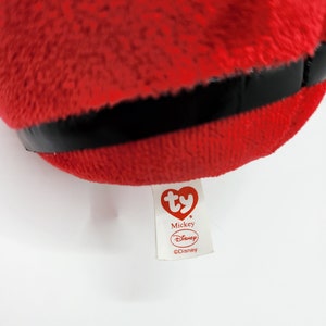 May include: Red plush Mickey Mouse toy with a black band around the middle. The toy has a white Ty tag with the words "Mickey" and "Disney" on it.