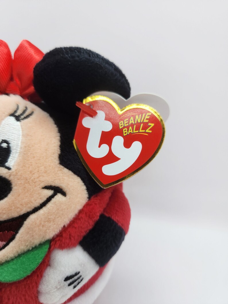 Puede incluir: Juguete de peluche rojo y negro de un rat&oacute;n de dibujos animados que lleva un vestido rojo y un lazo verde. El juguete tiene una etiqueta Ty Beanie Ballz.