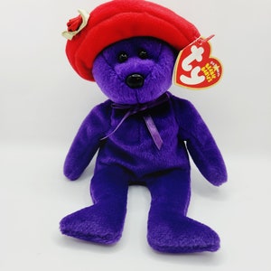 Peut inclure: Ours en peluche violet portant un béret rouge avec une étiquette Ty indiquant "Beanie Babies" et "Original".