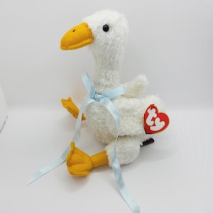May include: White plush goose with yellow beak and feet, wearing a blue ribbon around its neck. The goose has a red Ty tag attached to its back.