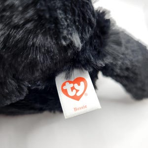 May include: Black plush toy with a white tag that says "ty" in a red heart and "Bessie" underneath.