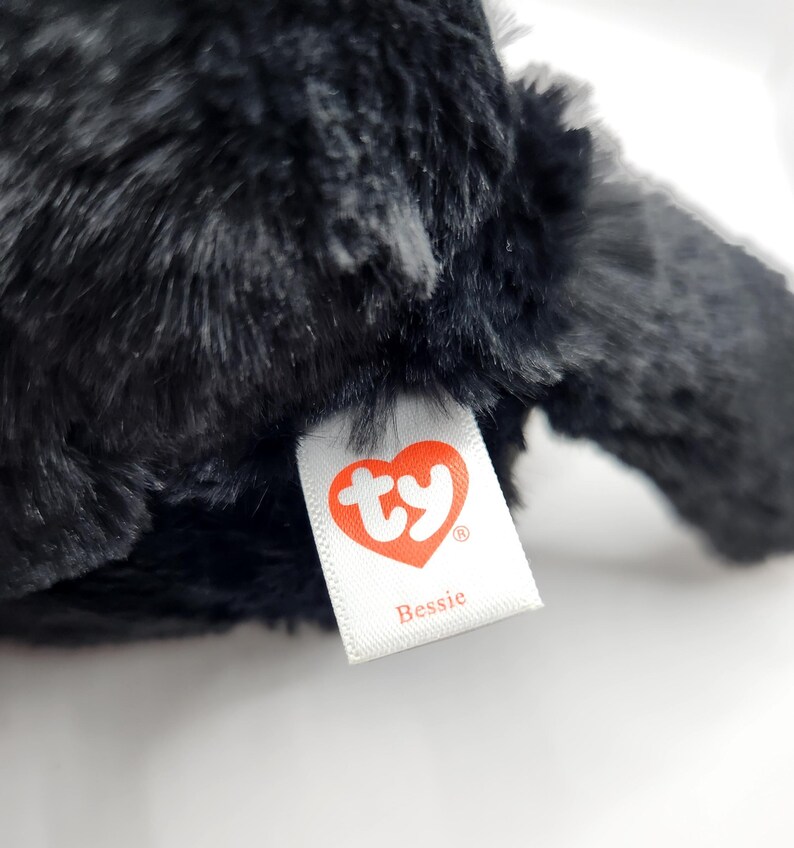 May include: Black plush toy with a white tag that says "ty" in a red heart and "Bessie" underneath.