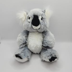 May include: A gray and white plush koala bear with black eyes and a black nose. The koala is sitting with its arms crossed and has a white belly.