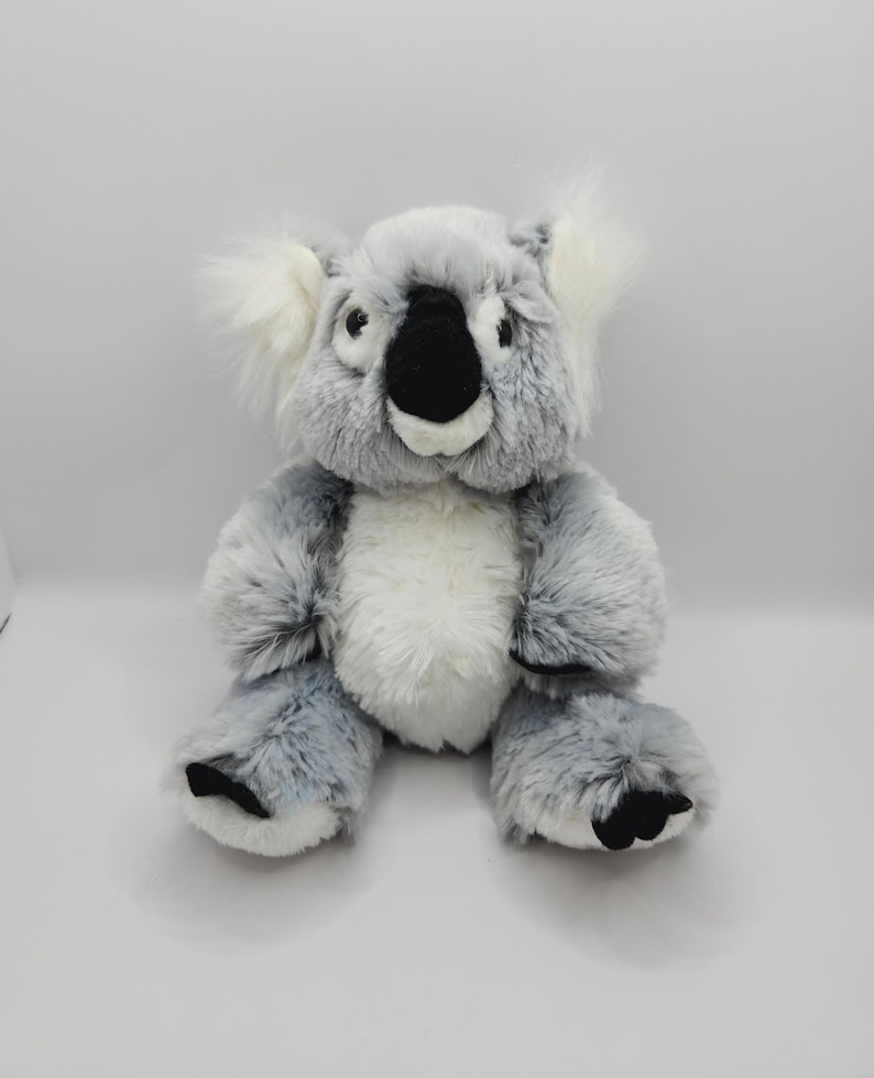 May include: A gray and white plush koala bear with black eyes and a black nose. The koala is sitting with its arms crossed and has a white belly.