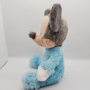 Peut inclure: Une peluche repr&eacute;sentant un personnage de souris, avec une t&ecirc;te et des oreilles grises, un museau rose et un corps bleu clair. Le jouet est assis, avec des d&eacute;tails blancs sur les mains et les pieds. Le jouet est con&ccedil;u pour ressembler &agrave; un personnage de dessin anim&eacute;.