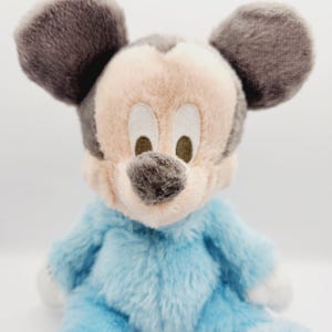 Peut inclure: Peluche de Mickey Mouse assis. Le jouet a un corps bleu clair, des mains et des pieds blancs, et un visage beige avec des oreilles et un nez gris fonc&eacute;. Les yeux sont brod&eacute;s. La peluche est douce et moelleuse.