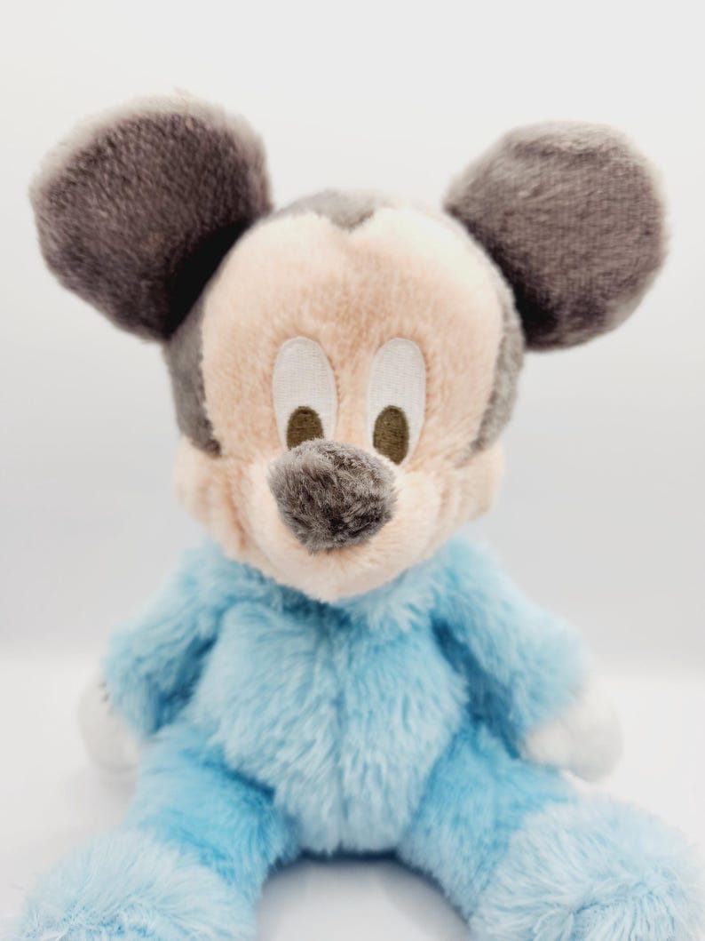 Peut inclure: Peluche de Mickey Mouse assis. Le jouet a un corps bleu clair, des mains et des pieds blancs, et un visage beige avec des oreilles et un nez gris fonc&eacute;. Les yeux sont brod&eacute;s. La peluche est douce et moelleuse.