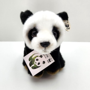 May include: A plush panda toy with black and white fur, dark eyes, and a black nose. It features a small, round, beige tag attached to its ear with a panda illustration and the text WWF, and a larger square tag with a green panda logo and text.