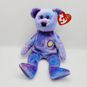 Può includere: Orso di peluche Beanie Baby tie-dye viola e blu con un nastro viola intorno al collo e un'etichetta Ty Beanie Babies attaccata all'orecchio.
