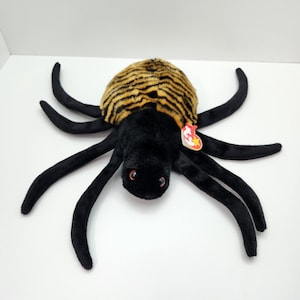 Może przedstawiać: Pluszowy pająk w czarno-żółte paski z czerwonymi oczami i czerwoną i białą metką Ty Beanie Babies.