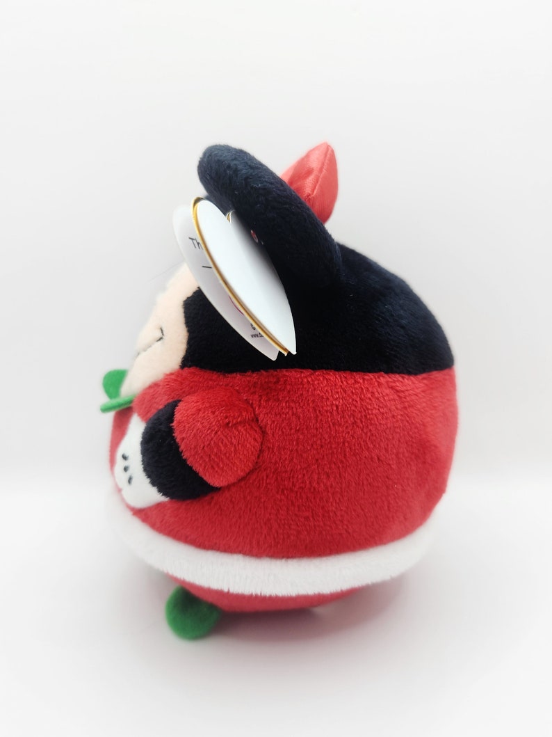 Puede incluir: Juguete de peluche rojo y negro con forma de personaje redondo que lleva un gorro de Pap&aacute; Noel. El juguete tiene un ribete blanco alrededor de la parte inferior y detalles verdes.