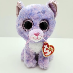 May include: A plush cat toy in shades of purple and pink. The cat has large, glittery eyes, pink nose, and whiskers. The ears have a sparkly pink lining. A red heart-shaped tag is attached.