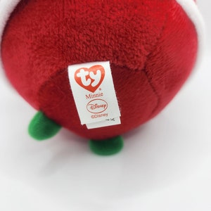 Puede incluir: Juguete de peluche rojo con forma de adorno navide&ntilde;o con la parte superior blanca y tallo verde. El juguete tiene una etiqueta Ty que dice "Minnie" y "Disney".