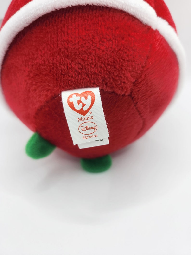 Puede incluir: Juguete de peluche rojo con forma de adorno navide&ntilde;o con la parte superior blanca y tallo verde. El juguete tiene una etiqueta Ty que dice "Minnie" y "Disney".