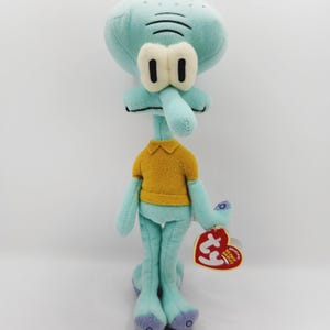 May include: A teal blue plush toy of Squidward Tentacles from the cartoon Spongebob Squarepants. He is wearing a yellow polo shirt and has a red Ty Beanie Baby tag attached to his arm.