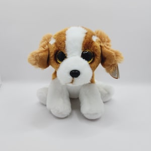 Peut inclure: Un jouet en peluche en forme de chien brun et blanc avec de grands yeux brillants. Le chien est assis, les pattes repliées sous son corps.