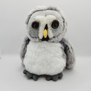 May include: A gray and white plush owl toy with black eyes and a yellow beak. The owl is sitting on a white background.