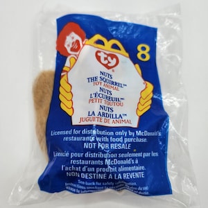 May include: A brown Ty Beanie Baby plush toy named "Nuts the Squirrel" in a clear plastic bag with a blue and white McDonald's Happy Meal wrapper. The wrapper has the Ty logo and the text "Licensed for distribution only by McDonald's restaurants with food purchase. Not for resale."