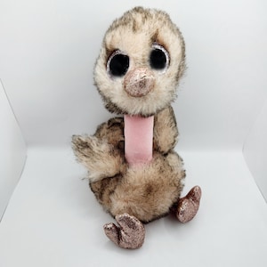 May include: A brown and tan plush ostrich with large black eyes and pink glitter accents. The ostrich is sitting with its legs crossed and has a pink neck.